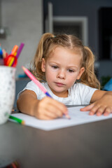 little girl draws with colored pencils in home. 