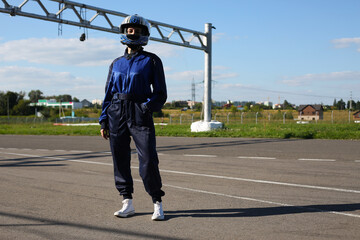 Young girl racer in a helmet stands near the track before the start of a karting race with her hand...