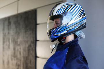 Girl kart racer in a helmet with a closed visor in profile in a racing garage