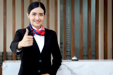 Portrait of happy smiling young beautiful Asian female receptionist in black suit standing and...