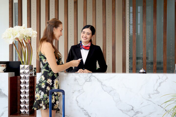 Beautiful smiling Asian female receptionist giving key card to tourist woman customer, female staff...