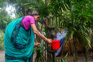 South asian rural aged woman collecting water from a tube well