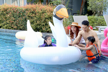 Naklejka premium Happy Asian family, father mother daughter and son enjoy outdoor activity at pool, kid and parent swimming with white swan plastic toy in blue water, relaxing family has fun together on summer holiday