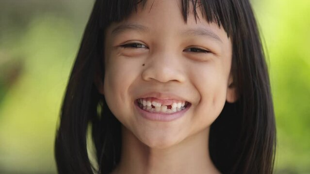 Close-up portrait of the bright face of Asian Thai kid girl aged 6 to 8 years, smiling beautifully, showing her growing teeth. She was a healthy and strong girl with beautiful long black hair.
