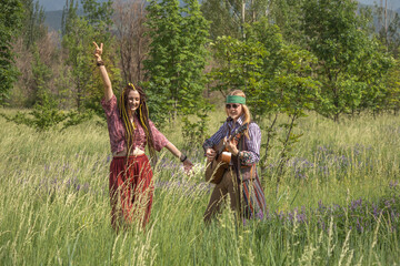 Couple of young people in hippie style. The girl is dancing, the guy is playing the guitar in a forest clearing on a sunny day
