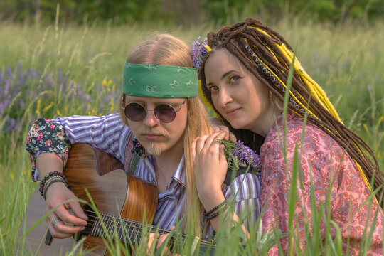 Guy and a girl in hippie style with a guitar are sitting in the grass on a forest glade. Close up