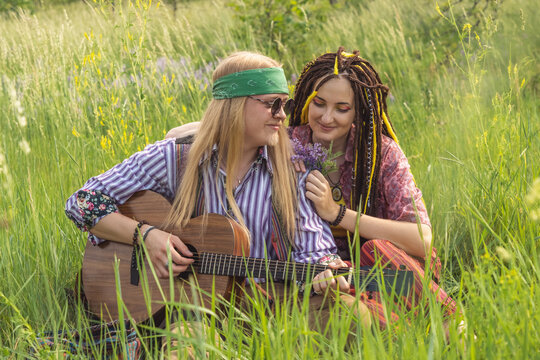 Guy and a girl in hippie style with a guitar are sitting in the grass on a forest glade on a sunny day