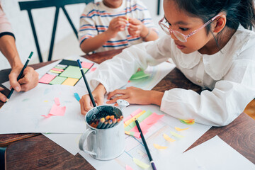 Happy school teacher and students having interesting engaging activities in class. Little children sitting around classroom table, talking and playing fun games together