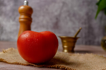 close-up of a fresh tomato with water drops on a raffia cloth with a mortar and pestle and pepper shaker in the background