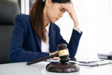Focus gavel with blur lawyer sitting at her desk with worried and exhausted expression, feeling...