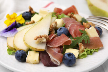 Tasty salad with brie cheese, prosciutto, walnuts and pear on white plate, closeup