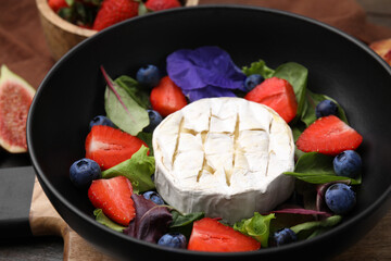 Delicious salad with brie cheese, blueberries and strawberries on table