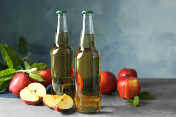 Delicious cider and apples with green leaves on gray table