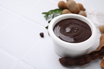 Bowl of tasty tamarind sauce and fresh pods on white table. Space for text