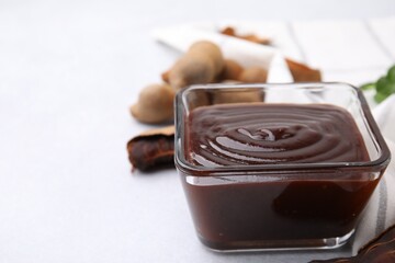 Bowl of tasty tamarind sauce and fresh pods on light table. Space for text
