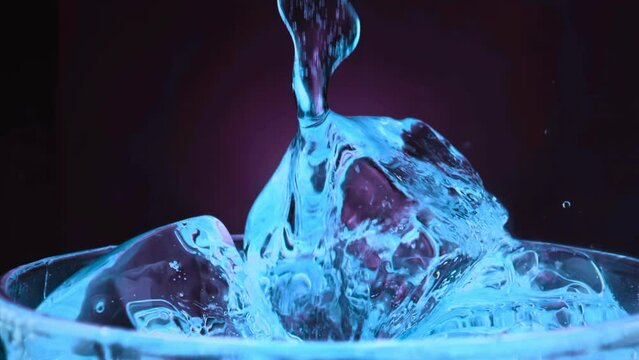 Super slow motion 1000fps on pours blue cocktail on red ice cubes in rotate glass.Slow motion pours blue alcohol on spin ice cubes in turn glass.Slow motion pours red ice cubes and alcohol cocktail