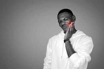 Sad millennial african american guy in hoodie presses hand to cheek, suffering from tooth pain