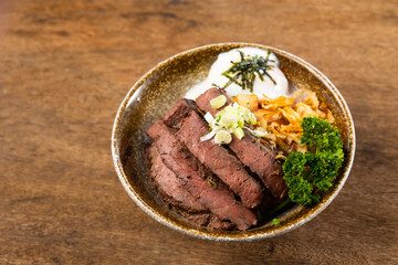Beef Bowl. bowl of white rice topped with slices of grill beef. Japanese food on restaurant table. Isolate on wood background