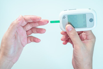 Close-up hand of pregnant woman checking her blood sugar level with glucometer and testing stripe...