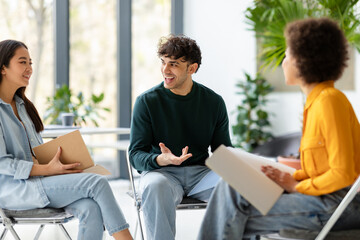 Three diverse enthusiastic friends classmates planning or discussing ideas, communicating in...