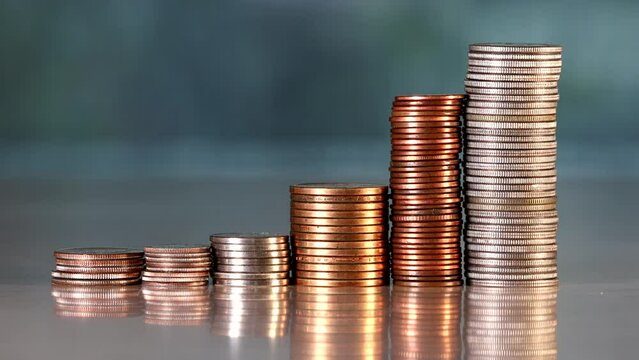 A hand adds coins to a stack on a table. 