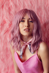 Happy young sexy Asian woman with pink wig hair and a short satin dress stands against a fur background in the studio. Fashion