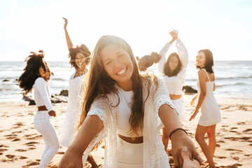 Group of diverse happy ladies having fun and dancing outdoors on the beach, celebrating...