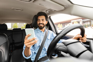 Cheerful indian man entrepreneur using cellphone while driving car