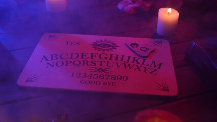 Close up shot of a wooden ouija board with a planchette on a table surrounded by candles,...
