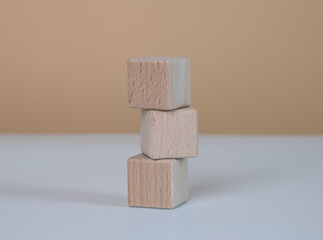 Three stacked light brown wooden cube blocks. on a white-brown background.
