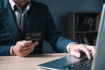 businessman uses a computer laptop and credit card to buy or purchase produce payment online and sits on the chair in the living room at home. The concept of finance and online shopping.