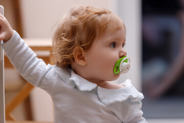 Cute little girl with a pacifier is standing in the children's room