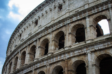 Fototapeta premium A close-up view of the Colosseum's exterior, highlighting the intricate details of the arches and stonework, with a hint of the Roman sky peering through, capturing the essence of ancient grandeur. 