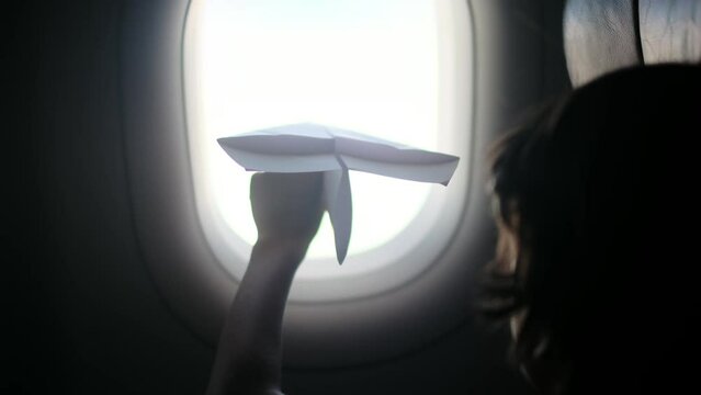 Young passenger playing paper airplane by airplane window, enjoying childlike wonder during flight, capturing carefree travel moment