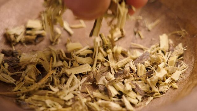 A hand takes crushed dried licorice root from a wooden dish in close up. An ingredient of traditional Chinese medicine