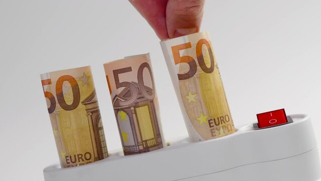 Consumer's hand removes a rolled up euro banknote from an electrical strip home outlet. Electricity discount concept