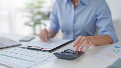 Close-up of business woman hand using a calculator and take notes to check company finances and...