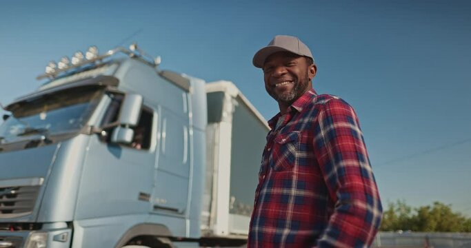 Portrait of happy african american employee standing and looking at camera. Attractive male truck driver in cap and shirt working at logistics company. Professional transportation concept.