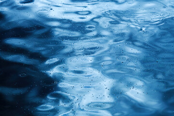 Rain drop circular pattern on rippled blue water surface, raindrops circles as abstract seasonal...