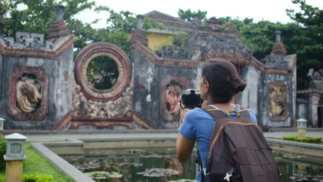 Young woman with camera and mobile phone captures images of an ancient city in Vietnam. Solo female summer adventures in Southeast Asia and Vietnam. Backpacker exploring world wonders.