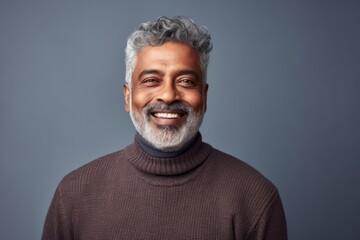 Obraz premium Medium shot portrait of an Indian man in his 60s against a minimalist or empty room background wearing a chic cardigan