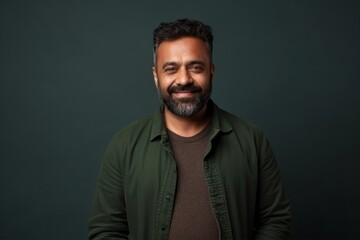 Fototapeta premium Medium shot portrait of an Indian man in his 40s against an abstract background wearing a chic cardigan