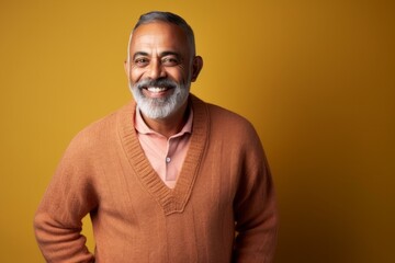 Fototapeta premium Portrait of a happy Indian man smiling at the camera against yellow background