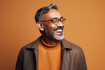 Fototapeta premium Portrait of a smiling indian man in eyeglasses against brown background
