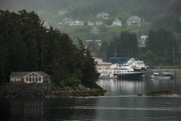 Fototapeta premium Grey, misty, foggy morning in archipelago near Sitka, Alaska with small islands channel cruising and houses