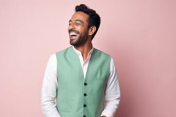 Fototapeta premium Portrait of a happy young indian man laughing against pink background