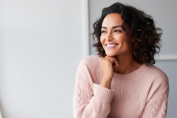 Medium shot portrait of an Indian woman in her 40s against a pastel or soft colors background wearing a cozy sweater