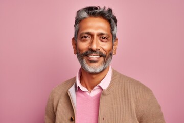 Obraz premium Portrait of happy mature Indian man looking at camera and smiling, standing against pink background