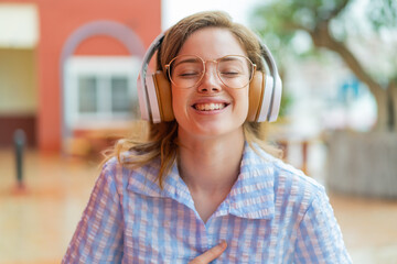 Young redhead girl headphones at outdoors smiling a lot