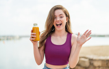Young redhead girl holding an orange juice at outdoors with shocked facial expression